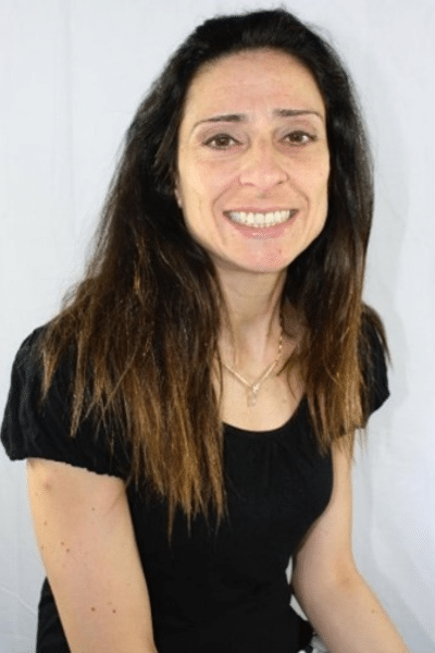 A headshot of Betul. She is wearing a black shirt and is smiling widely.